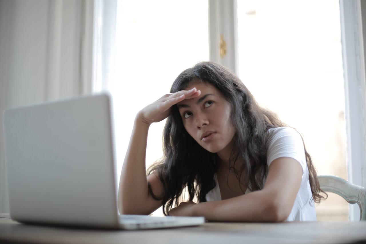 Fotografia de mulher mexendo no computador com mão na testa e rosto aborrecido simbolizando irritabilidade