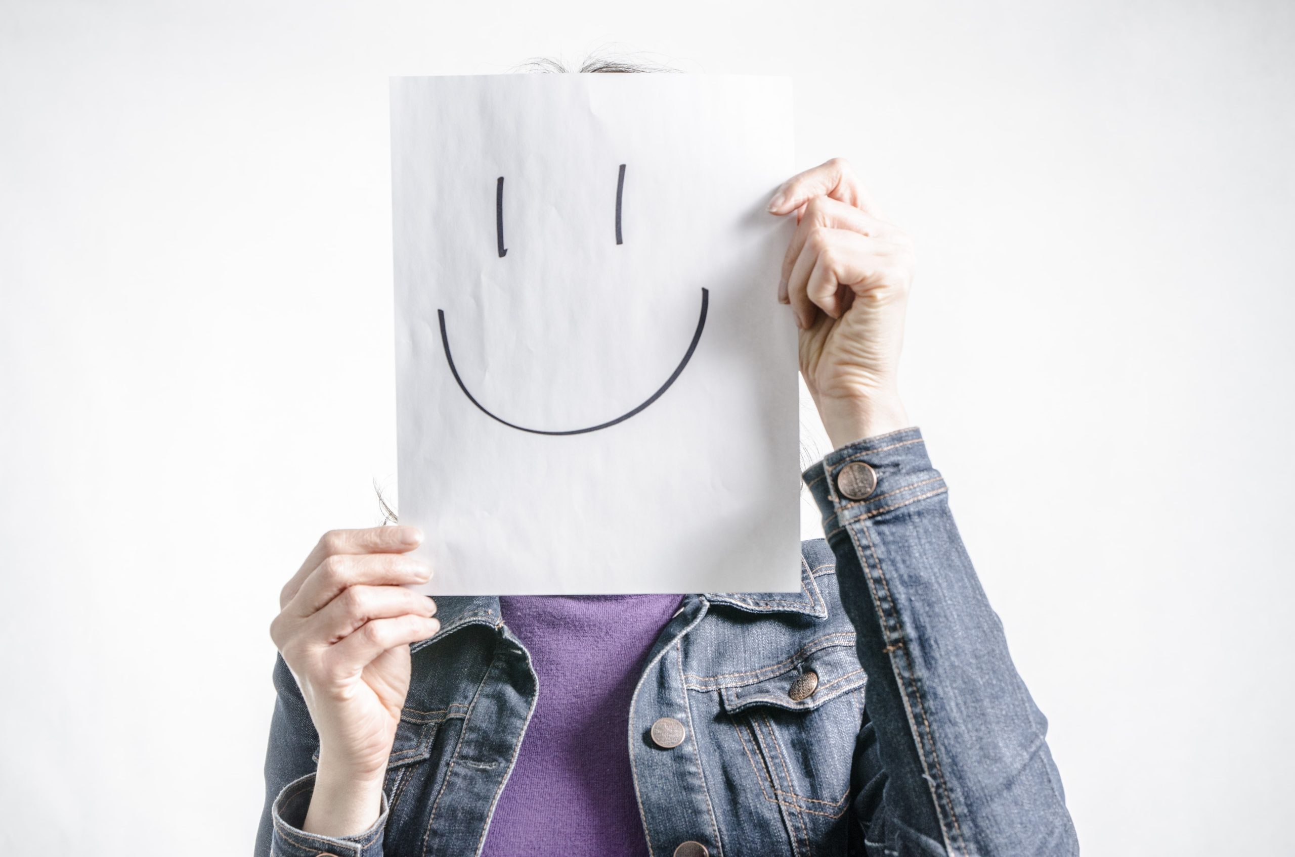 Pessoa segurando uma folha de papel com um rosto feliz desenhado em frente ao seu próprio.